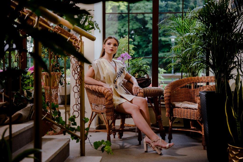Modelka siedząca na wiklinianym krześlew pomieszczeniu pełnym kwiatów doniczkowychpe